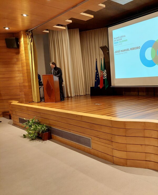 Um orador em palco, com apresentação sobre Valongo ao fundo.