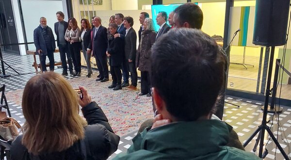 Grupo de pessoas posando para uma foto, com um segurança ao fundo.