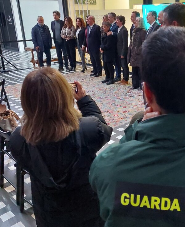 Grupo de pessoas posando para uma foto, com um segurança ao fundo.