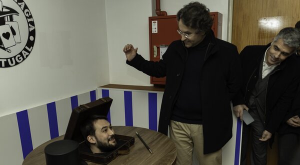 Um mágico apresenta um truque com uma caixa e cartas, enquanto espectadores observam.