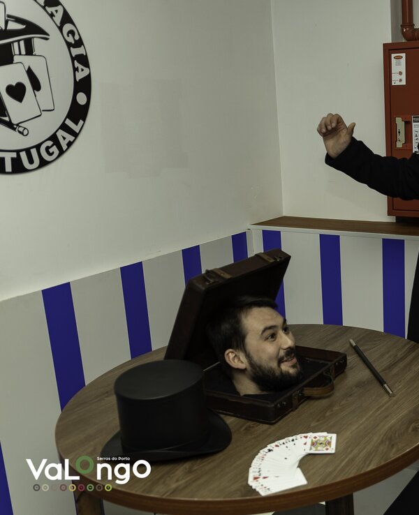 Um mágico apresenta um truque com uma caixa e cartas, enquanto espectadores observam.