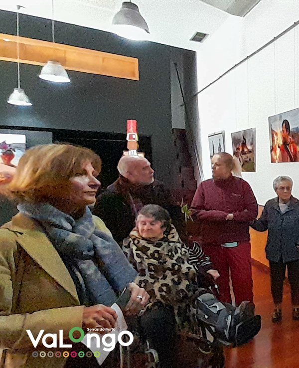 Grupo de pessoas a ouvir um guia numa galeria de arte com fotografias.