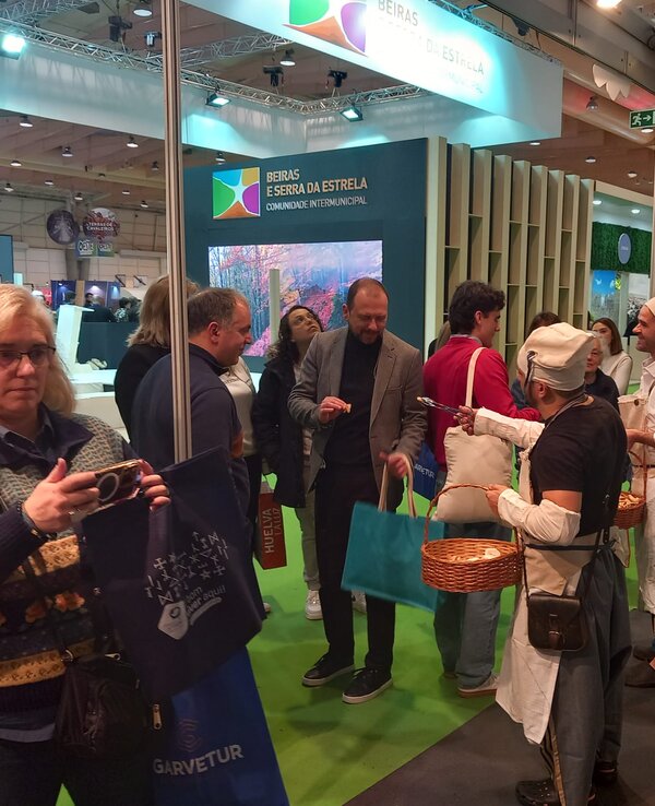 Grupo de pessoas interagindo em um evento, com um expositor ao fundo.