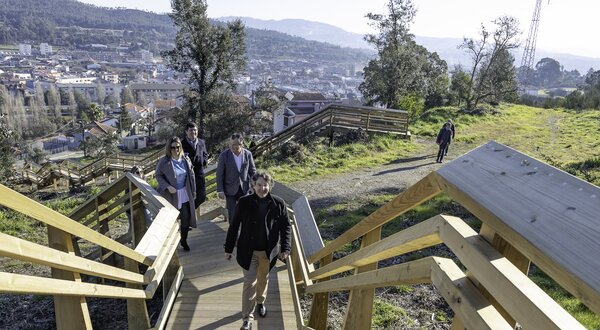 Grupo de pessoas a descer escadas de madeira em área verde com vista para a cidade.