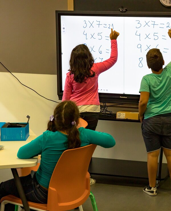 Crianças a resolver problemas matemáticos em quadro interativo.