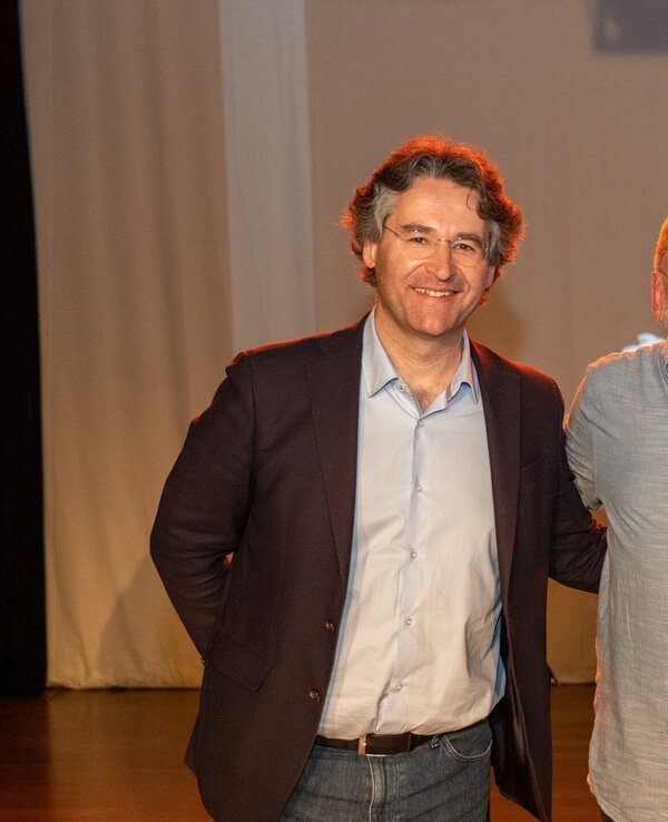 Três homens posam juntos em um palco, com um fundo neutro.