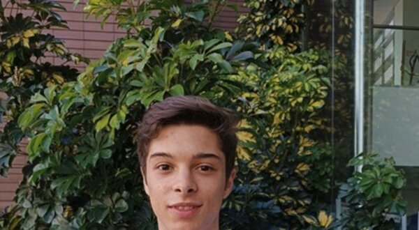 Jovem em bata branca, com crachá, em frente a plantas verdes.