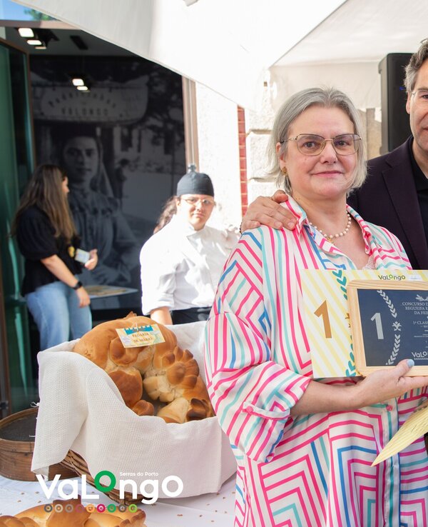 Uma mulher com um prémio em mãos, ao lado de um homem, rodeados por pessoas.