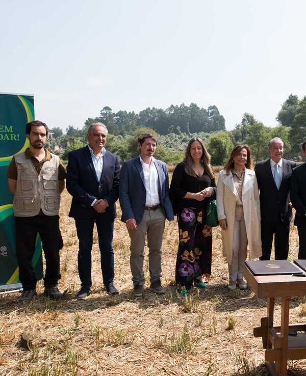 Grupo de pessoas em campo, com mesa e documentos, rodeados pela natureza.