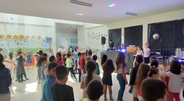 Crianças dançando numa festa escolar com música e luzes coloridas.