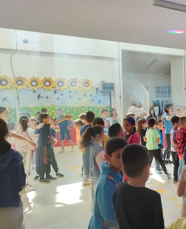 Crianças dançando numa festa escolar com música e luzes coloridas.