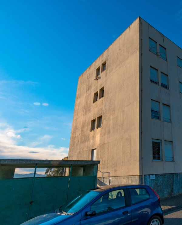 Edifício de betão com janelas grandes, céu azul ao fundo e um cão na rua.