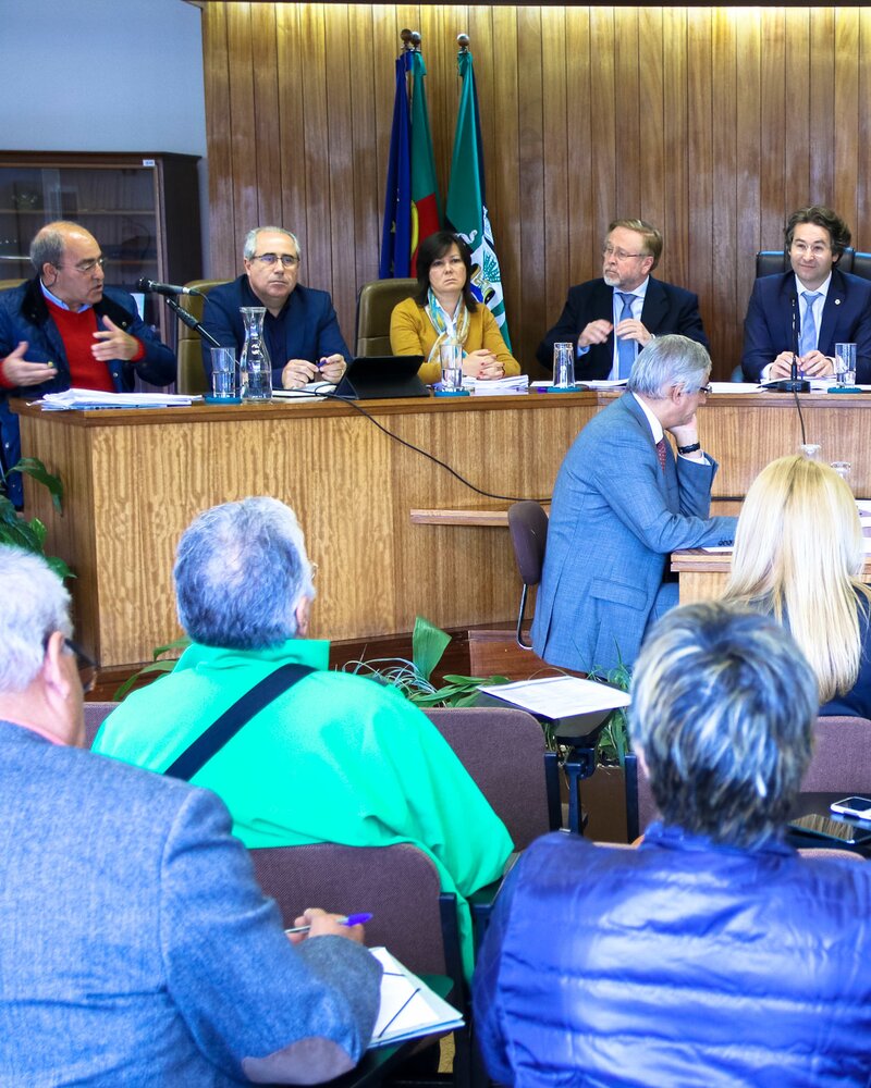 Reunião com várias pessoas sentadas em mesa, discutindo assuntos importantes.