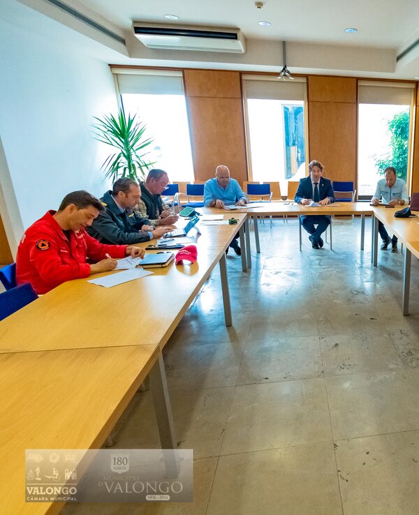 Reunião com várias pessoas sentadas à volta de uma mesa em ambiente de escritório.