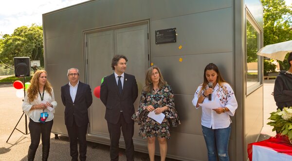 Grupo de pessoas em evento ao ar livre, junto a um quiosque metálico.