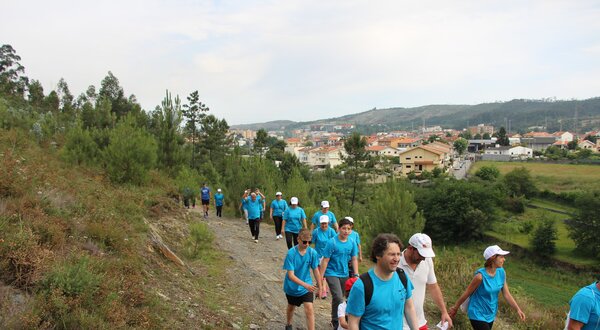 Grupo de pessoas a caminhar numa trilha, vestidas com camisetas azuis.