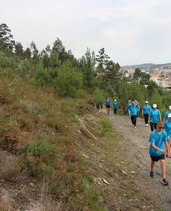 Grupo de pessoas a caminhar numa trilha, vestidas com camisetas azuis.