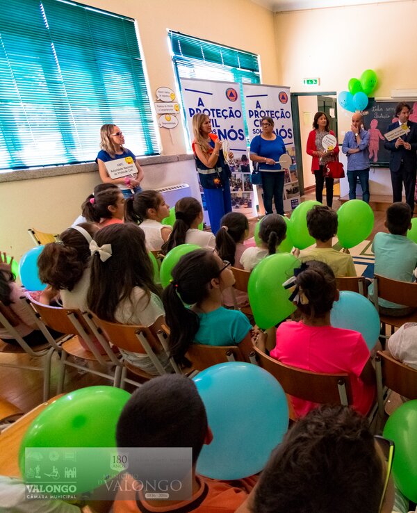 Evento escolar com crianças e adultos, balões verdes e apresentações.