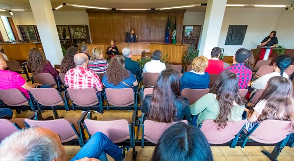 Público assistindo a uma apresentação em um auditório, com intérprete de língua gestual.