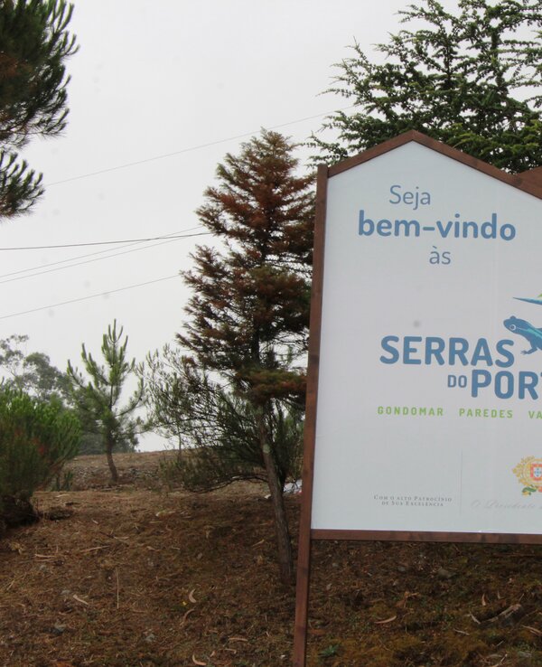 Placa de boas-vindas às Serras do Porto, com árvores ao fundo.