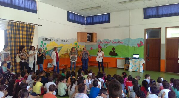 Grupo de pessoas a apresentar numa sala cheia de crianças sentadas.