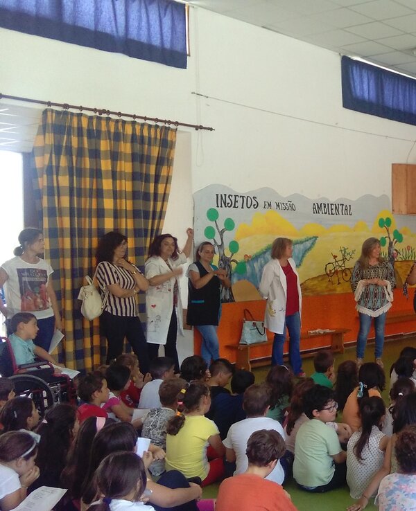 Grupo de pessoas a apresentar numa sala cheia de crianças sentadas.