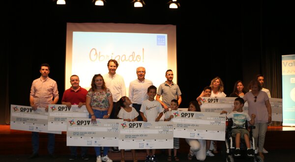 Grupo de pessoas a segurar grandes cheques em evento de agradecimento.