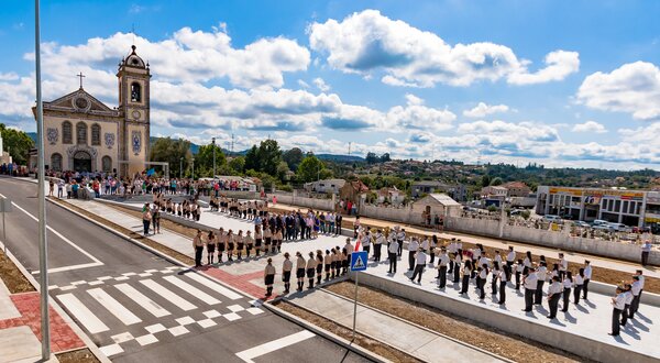Desfile em frente a uma igreja, com pessoas alinhadas na rua.