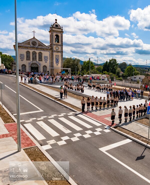 Desfile em frente a uma igreja, com pessoas alinhadas na rua.
