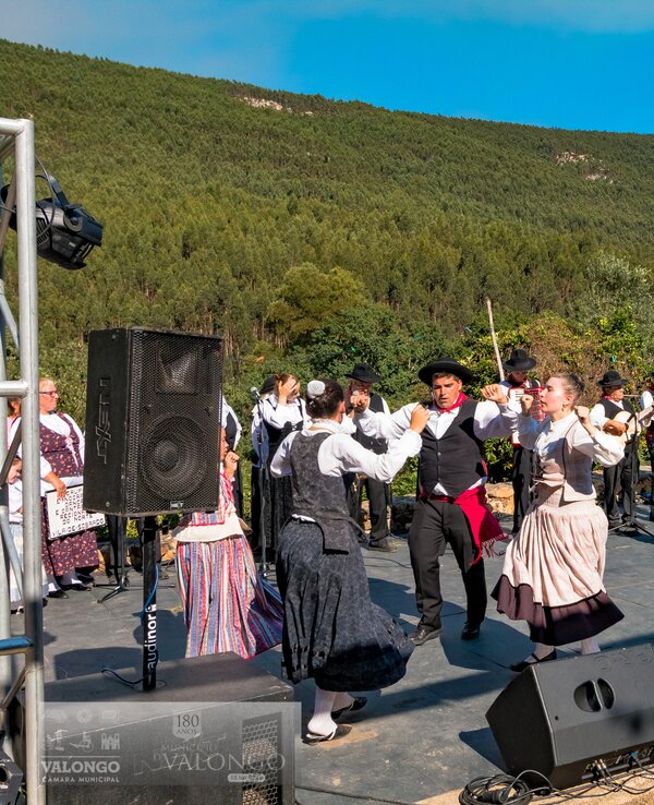 Grupo de dançarinos em trajes tradicionais a dançar ao ar livre.