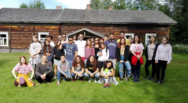 Grupo de jovens sorridentes posando em frente a uma casa de madeira.