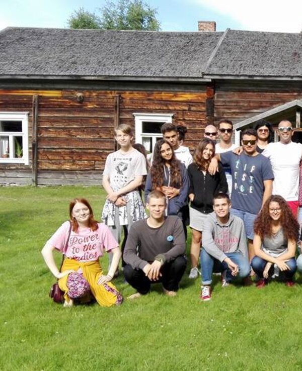 Grupo de jovens sorridentes posando em frente a uma casa de madeira.