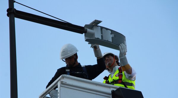 Dois trabalhadores em plataforma elevatória a instalar um equipamento no poste.