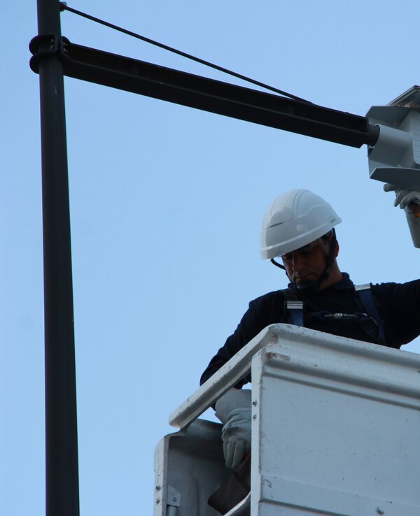 Dois trabalhadores em plataforma elevatória a instalar um equipamento no poste.