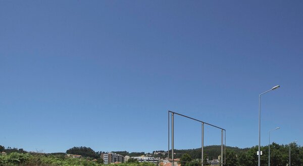 Vista de um terreno vazio com estrutura metálica e céu azul ao fundo.