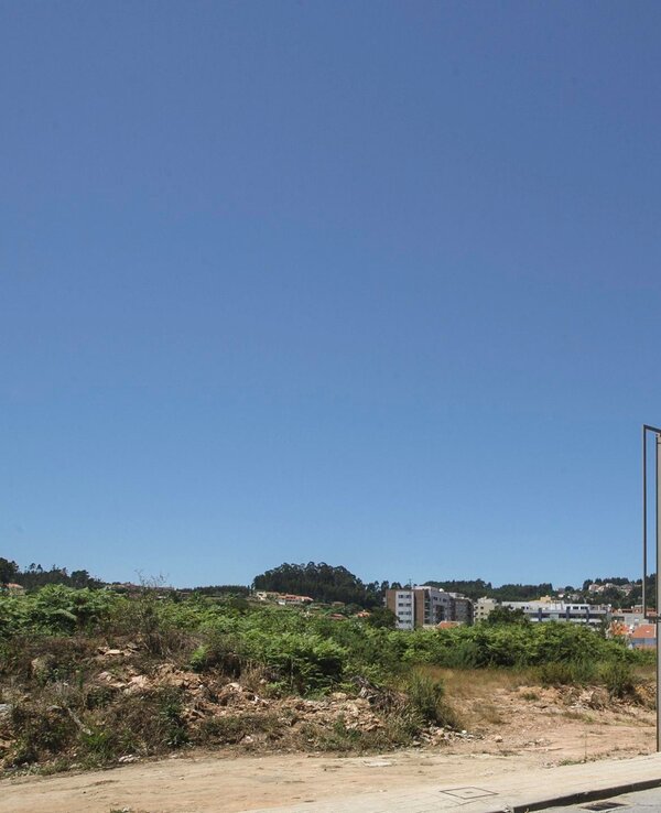 Vista de um terreno vazio com estrutura metálica e céu azul ao fundo.