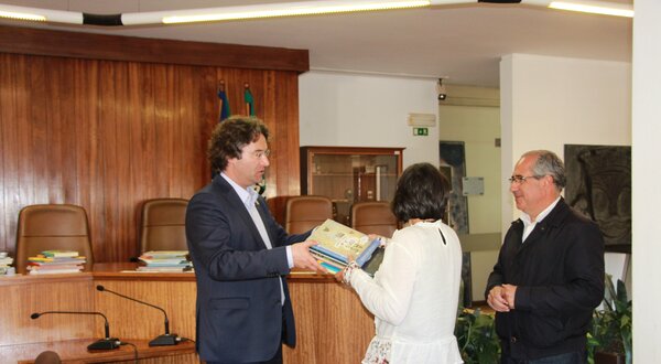 Um homem entrega um livro a uma mulher em um ambiente formal.