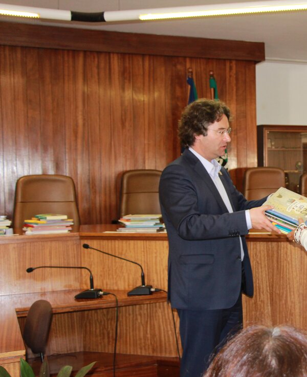 Um homem entrega um livro a uma mulher em um ambiente formal.
