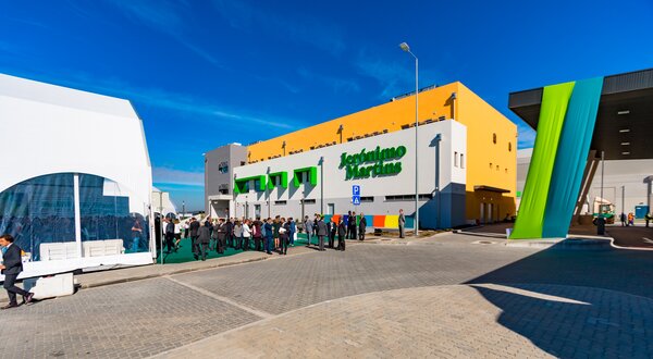 Edifício moderno com pessoas em fila, céu azul e decoração colorida.