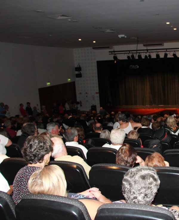 Público sentado em um auditório, assistindo a uma apresentação no palco.