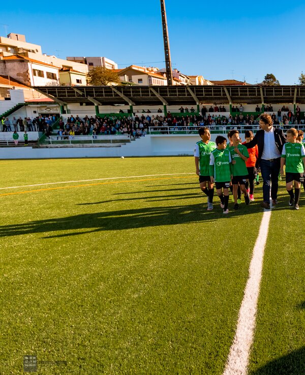 Crianças em campo de futebol, vestidas de verde, a caminho da bancada cheia.