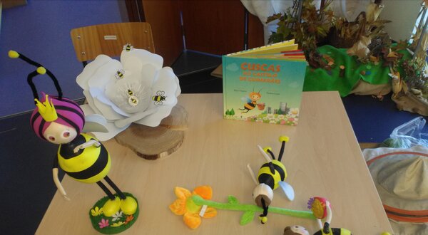 Mesa com bonecos de abelhas, flor branca e livro sobre polinização.