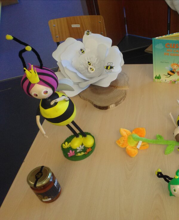 Mesa com bonecos de abelhas, flor branca e livro sobre polinização.