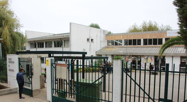 Entrada de uma escola com portão verde e edifícios ao fundo.