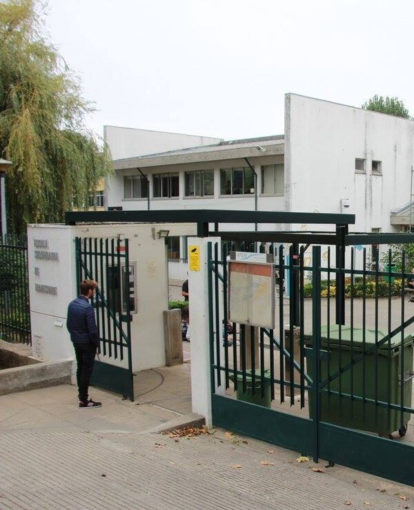 Entrada de uma escola com portão verde e edifícios ao fundo.