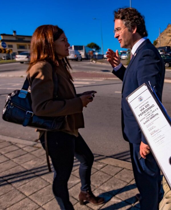 Uma mulher com colete amarelo segura um folheto enquanto conversa com duas pessoas.