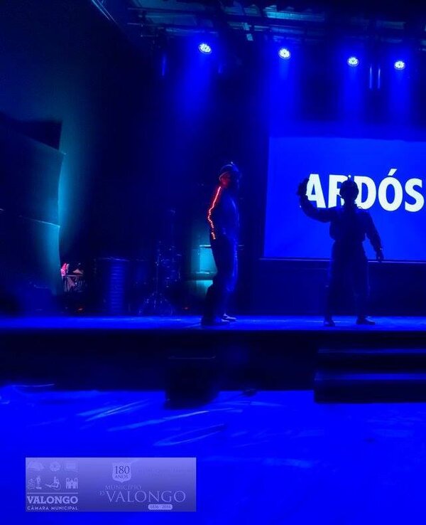 Três dançarinos em palco iluminado com luzes azuis, apresentando 'AFDÓSIA'.