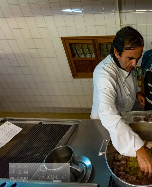 Dois homens a cozinhar em uma cozinha, um a adicionar temperos à carne.