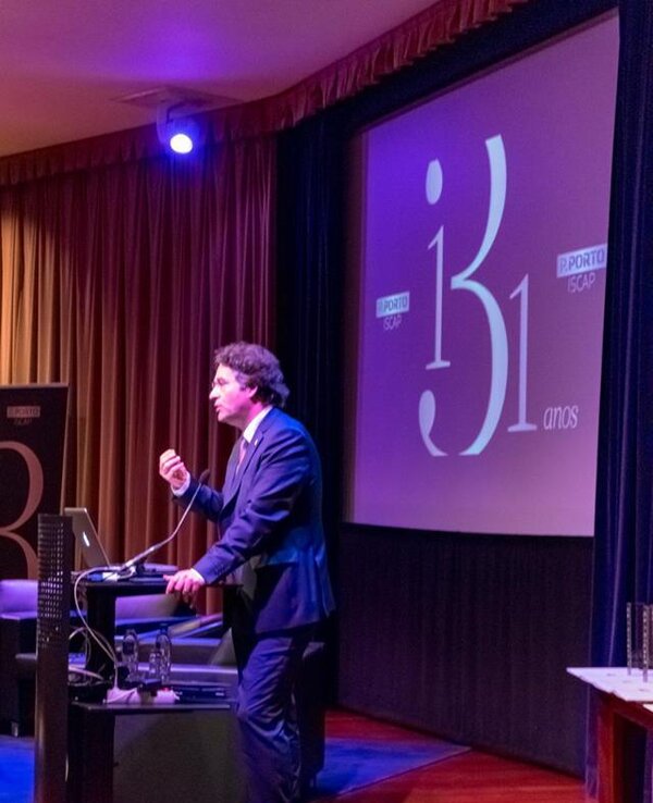 Homem em fato a apresentar num evento, com um ecrã ao fundo a dizer '31 anos'.