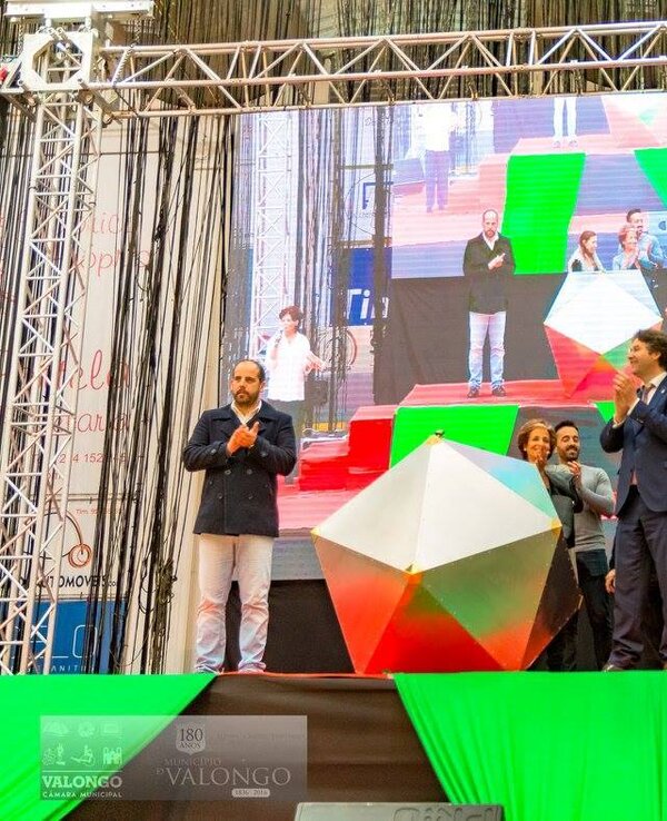 Grupo de pessoas aplaudindo em palco, com um grande ecrã atrás.